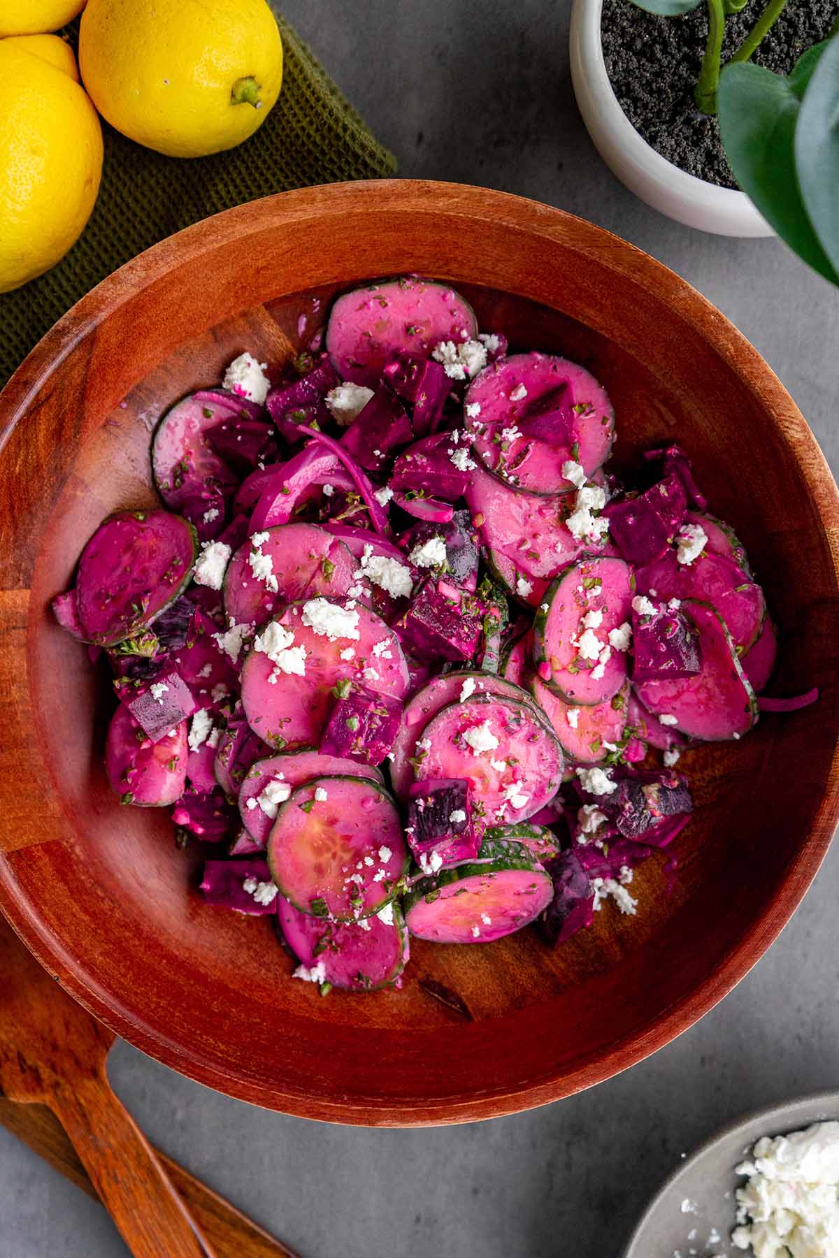 Beetroot and cucumber salad in a wood bowl with feta on top. Lemons are on the side