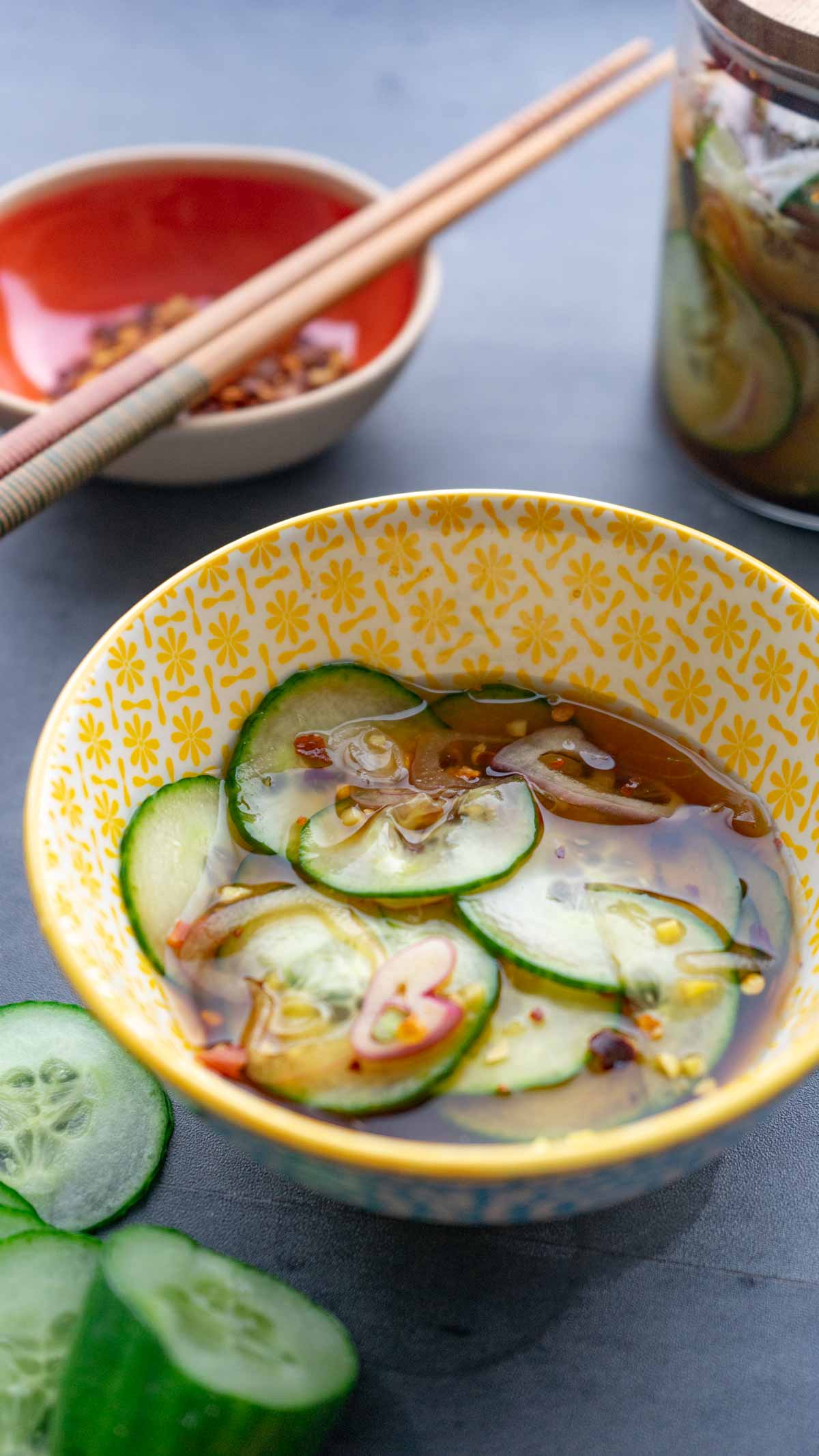 Asian Pickled Cucumbers in a small yellow bowl with cut cucumbers surrounding the bowl