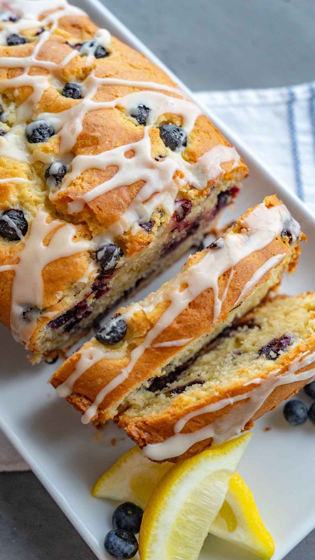 gluten free lemon blueberry bread on a rectangle white serving plate drizzled with lemon icing