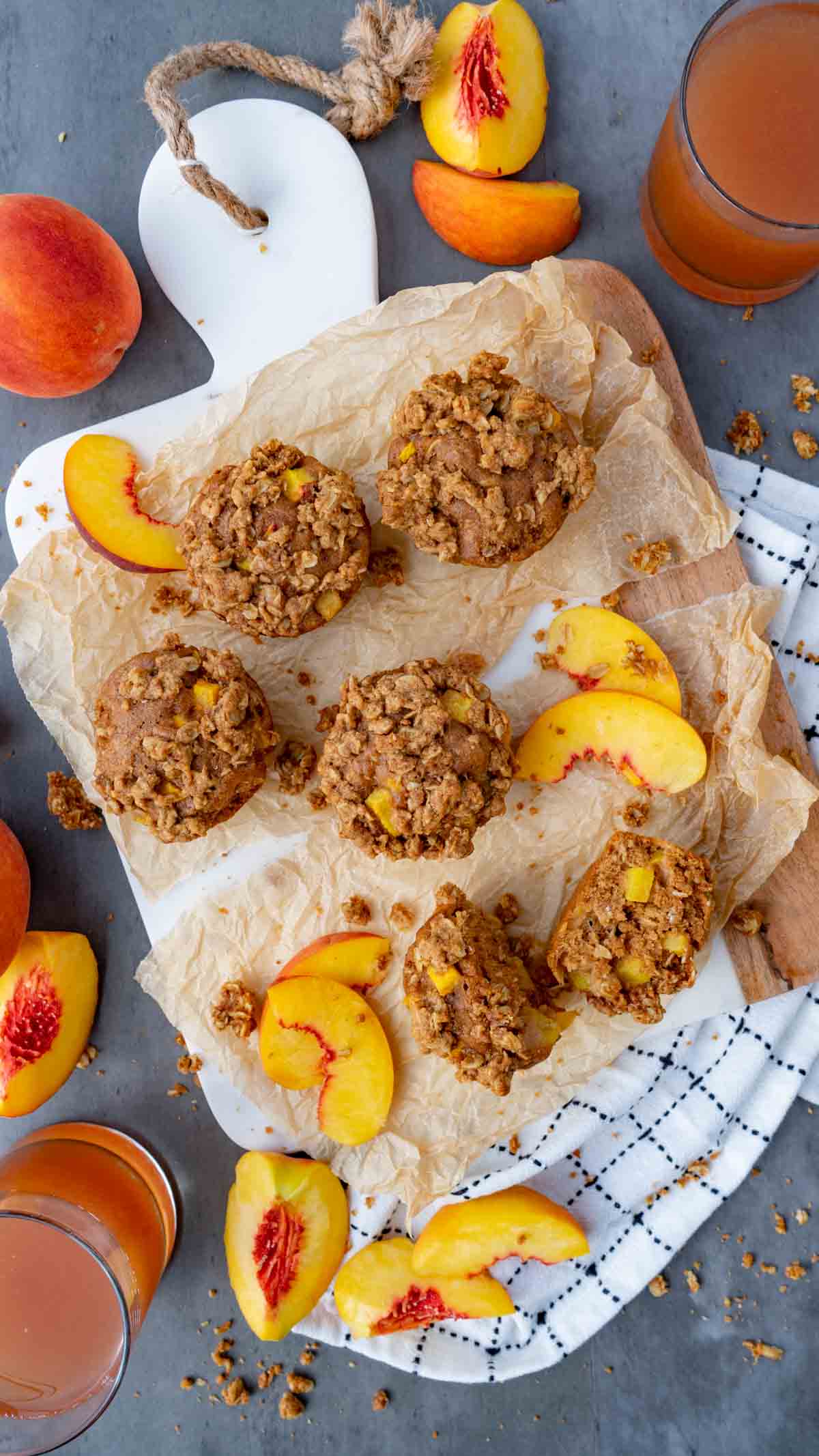 peach cobbler muffins on a cutting board with brown parchment paper surrounded by peaches