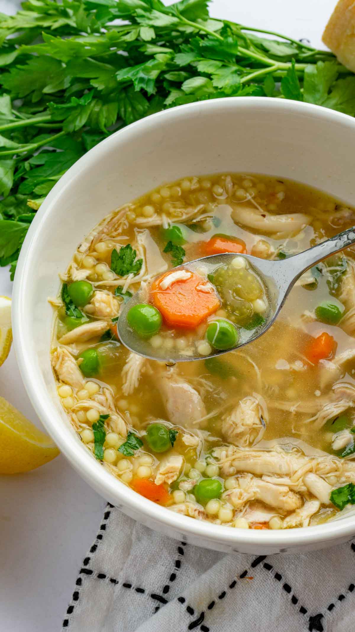 Italian Penicillin Soup in a white bowl with herbs, lemons, and a white kitchen towel surrounding it